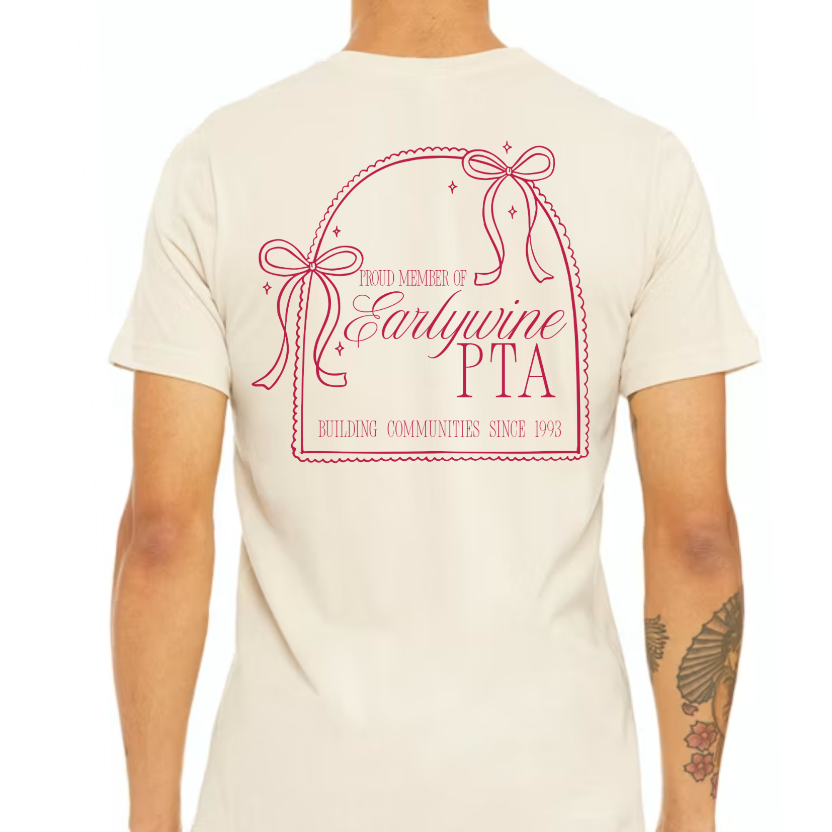 Back view of a cream-colored t-shirt featuring a large pink bow-inspired Community Bow design with customizable organization, member, and leadership text.