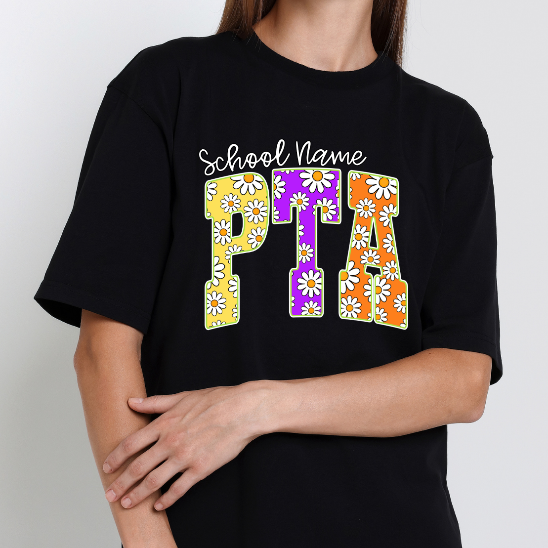 Black t-shirt featuring colorful daisy-pattern PTA lettering in yellow, purple, and orange with optional school name personalization.